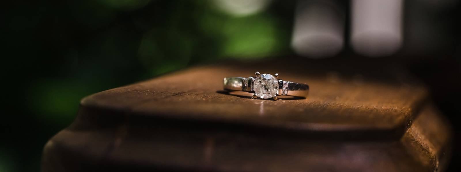 Close-up of a diamond ring resting on a wooden surface with a blurred green background.