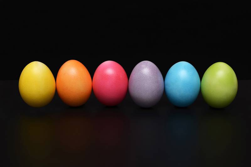 Six vibrant eggs in orange, pink, blue, green, purple, and yellow on a dark surface.