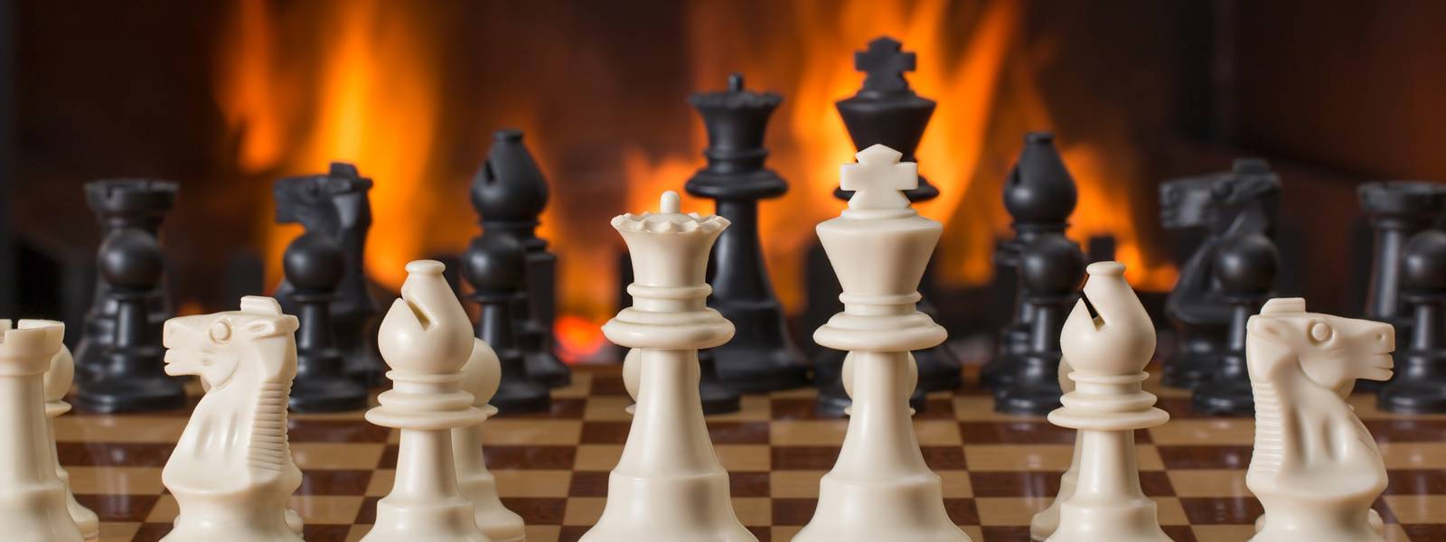 Chess pieces arranged on a board with a glowing fireplace behind.