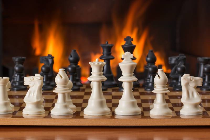 Chess pieces arranged on a board with a glowing fireplace behind.