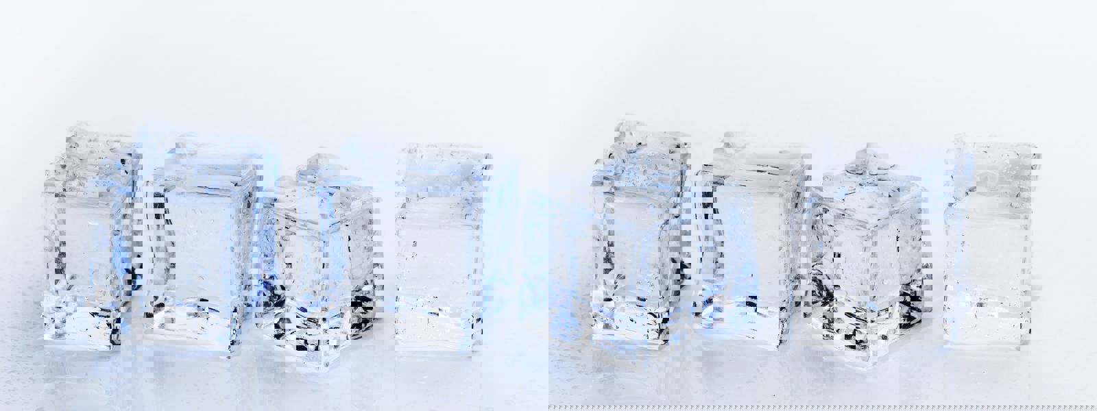 Four clear ice cubes on a reflective surface with droplets of water.