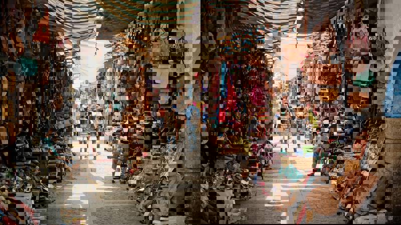 Busy market street lined with colourful bags and handmade crafts.