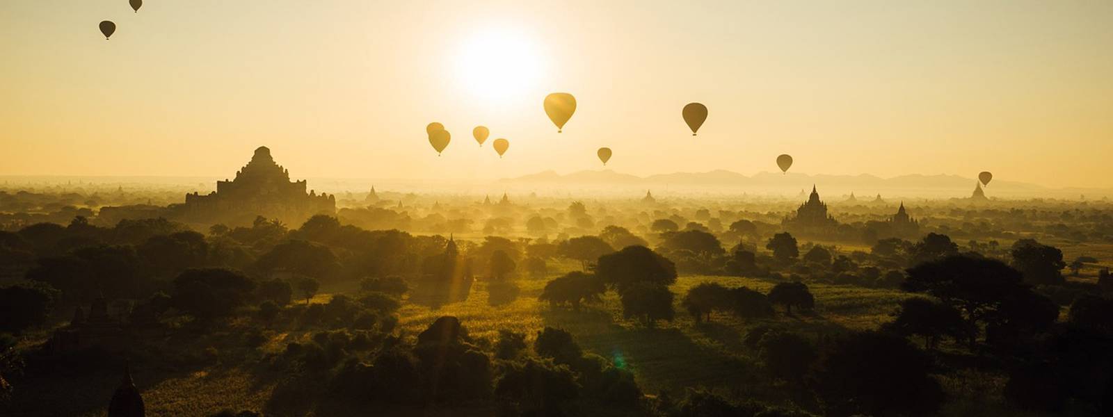 Hot air balloons over a misty landscape at sunrise, with ancient temples in the background.