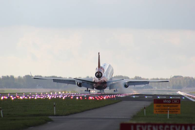 Commercial aircraft approaching runway, illuminated by landing lights.