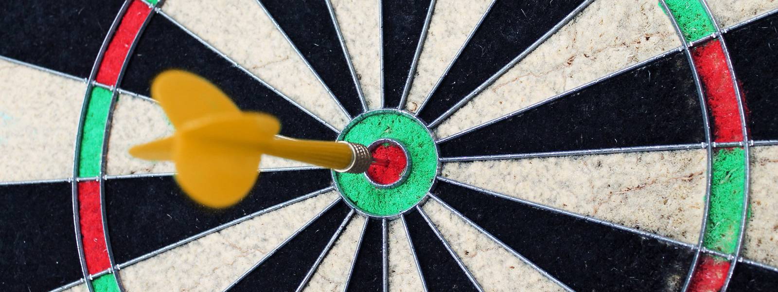 Close-up of a dartboard with a yellow dart in the bullseye.