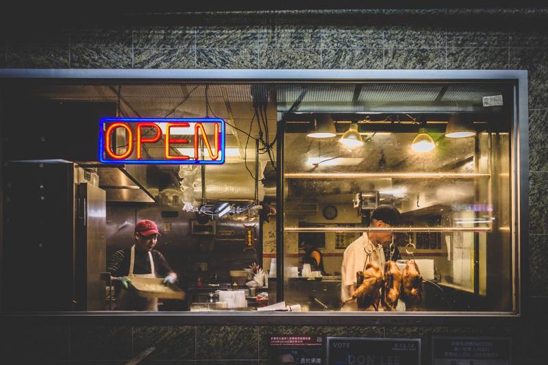 Two chefs working in a restaurant kitchen with an illuminated 'OPEN' sign.