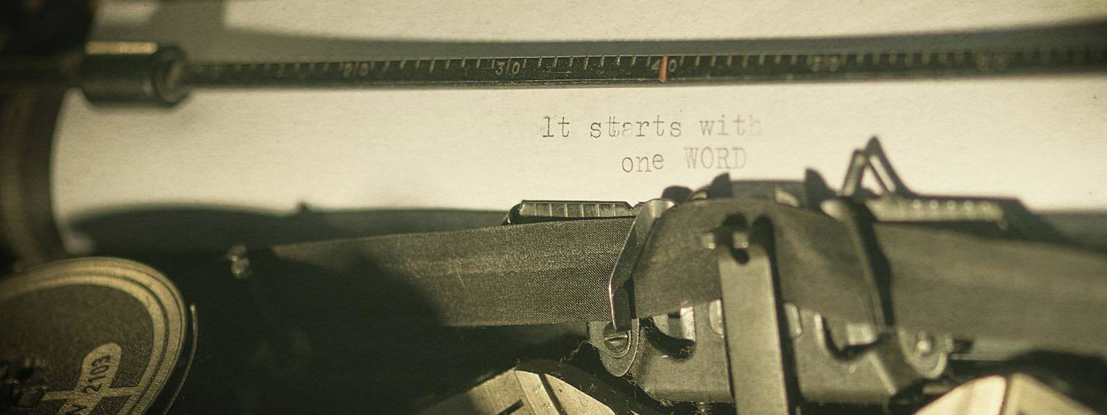 Close-up of a typewriter with the text 'It starts with one WORD' on paper.