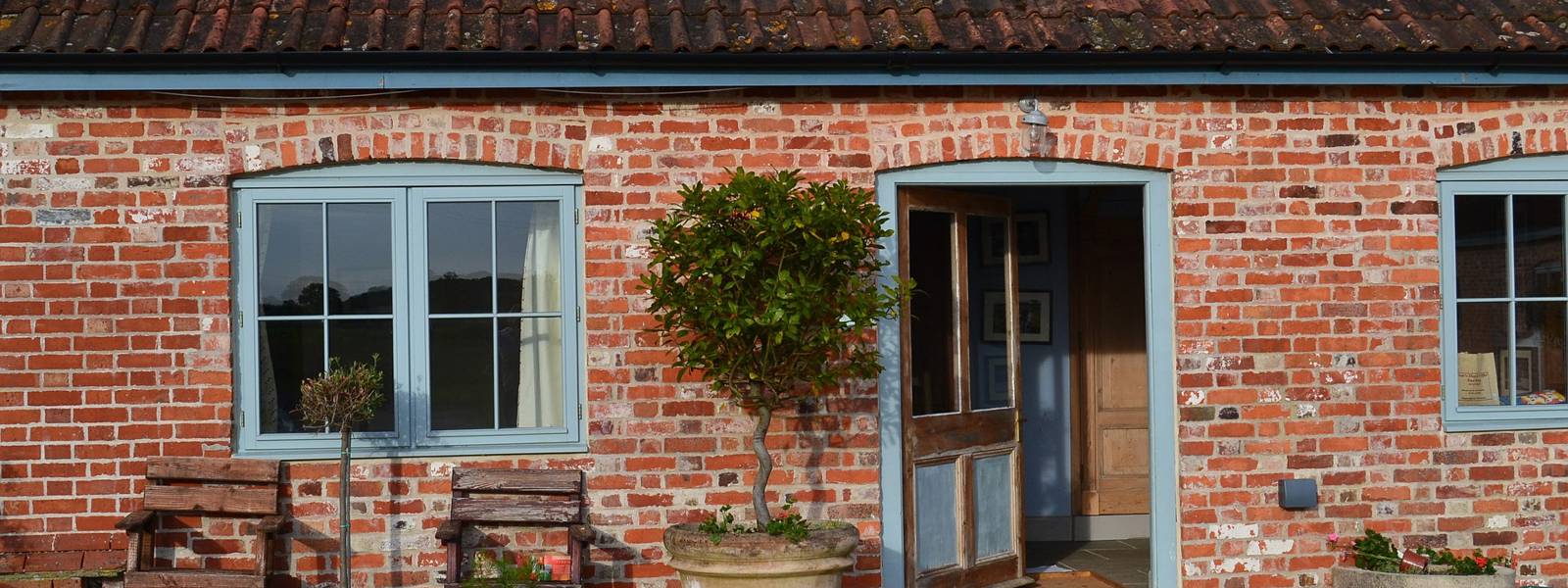 Charming brick cottage entrance with potted plants and wooden benches.