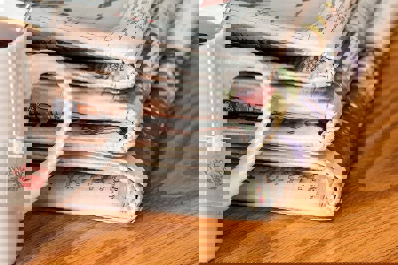 A stack of newspapers beside a cup of tea on a wooden table.