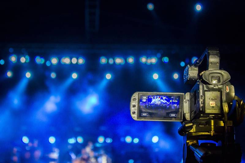 Video camera focused on a concert stage illuminated by blue lighting.