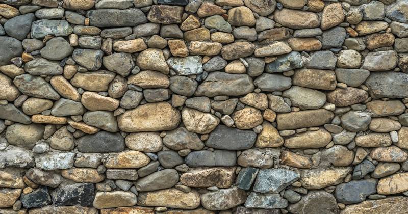 A textured wall made of various sizes of smooth, rounded stones.